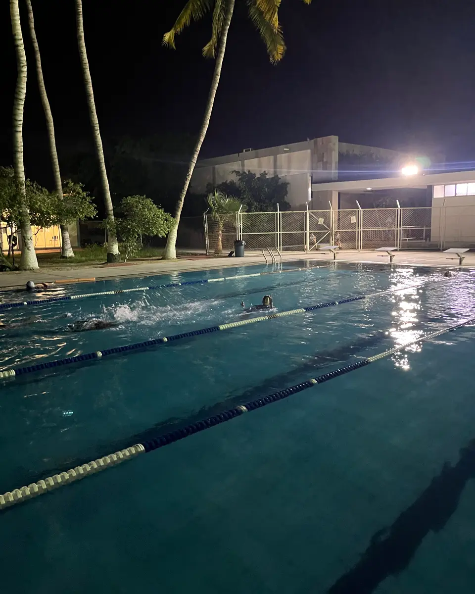 Nadadores entrenando de noche en una alberca iluminada